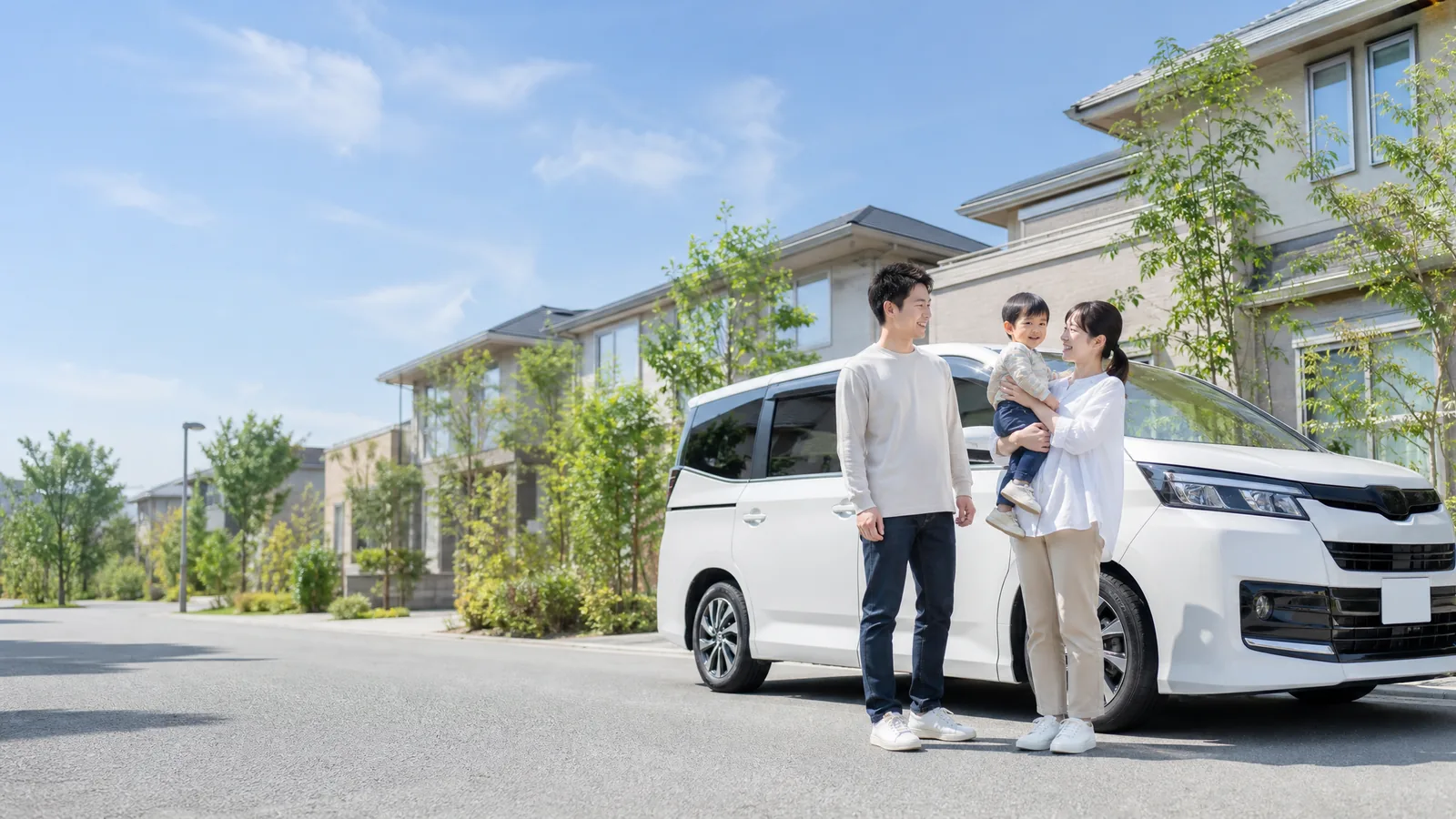 住宅街で白いミニバンの前に立つ家族